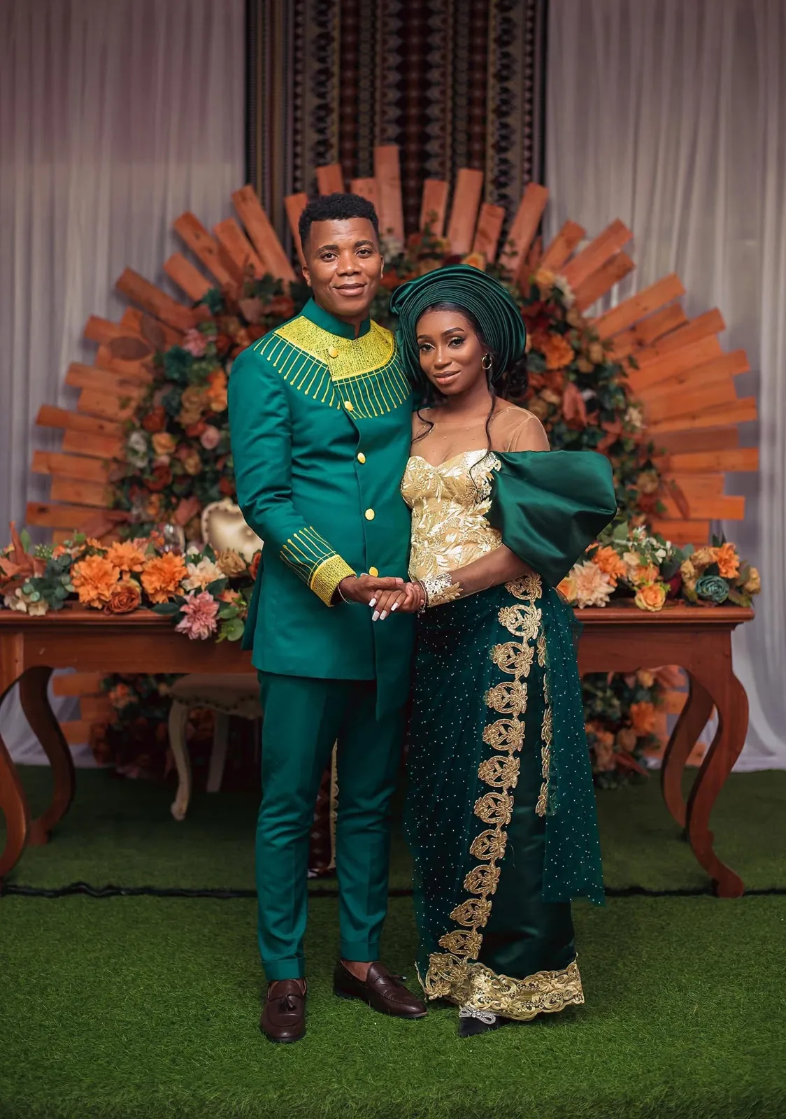 Casal em trajes verde e dourado diante da decoração